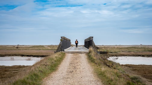 A man walking across the Bailey Bridge on Orford Ness with headphones on